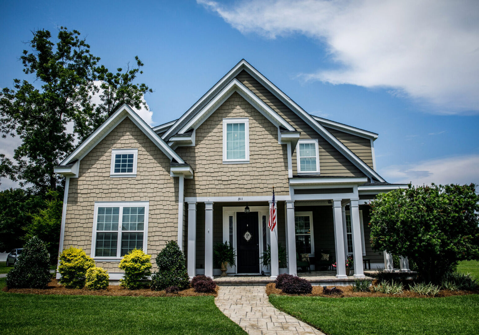 Large tan new construction home with a walkway in the suburbs